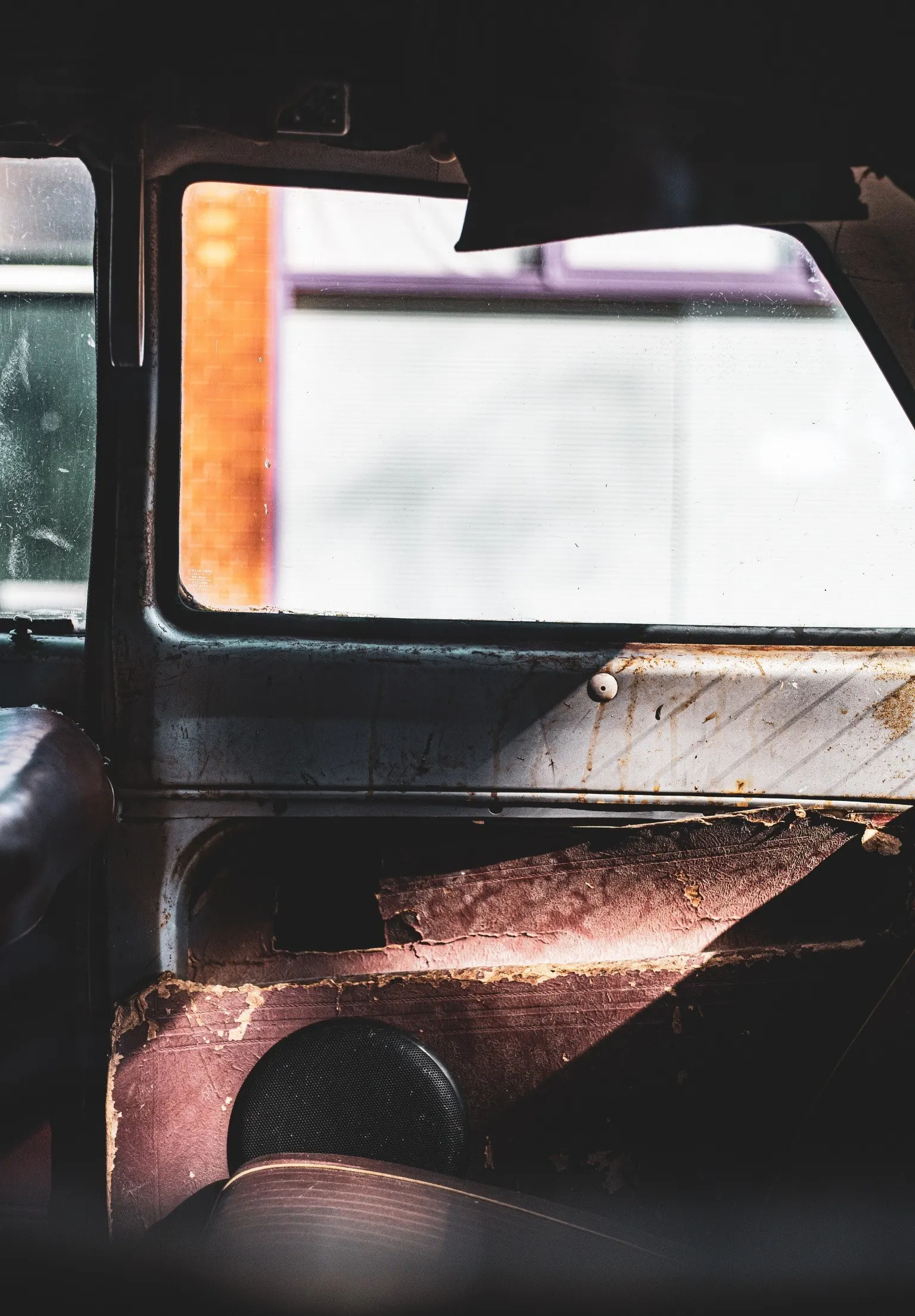 View through the window of an old car, with a rusted interior and a strip of sunlight