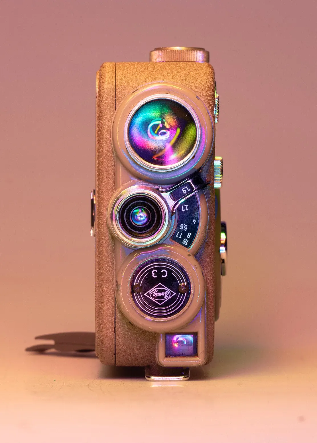Vintage film camera with three lenses in pink and purple light, on a pastel background