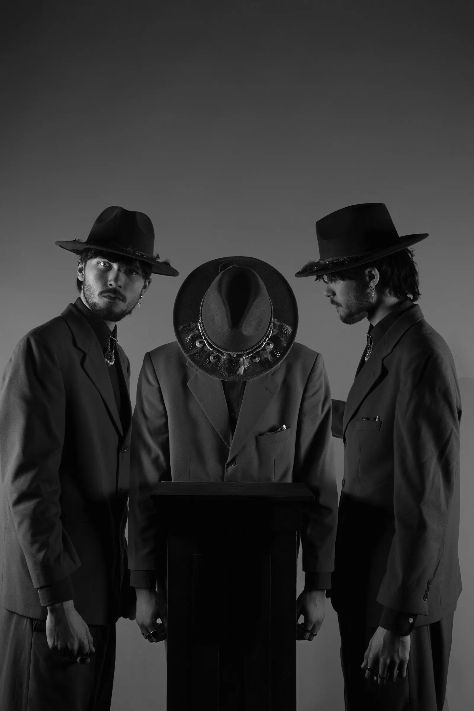 Black and white photo of three men in suits and hats around a table, the one in the middle with his head bowed
