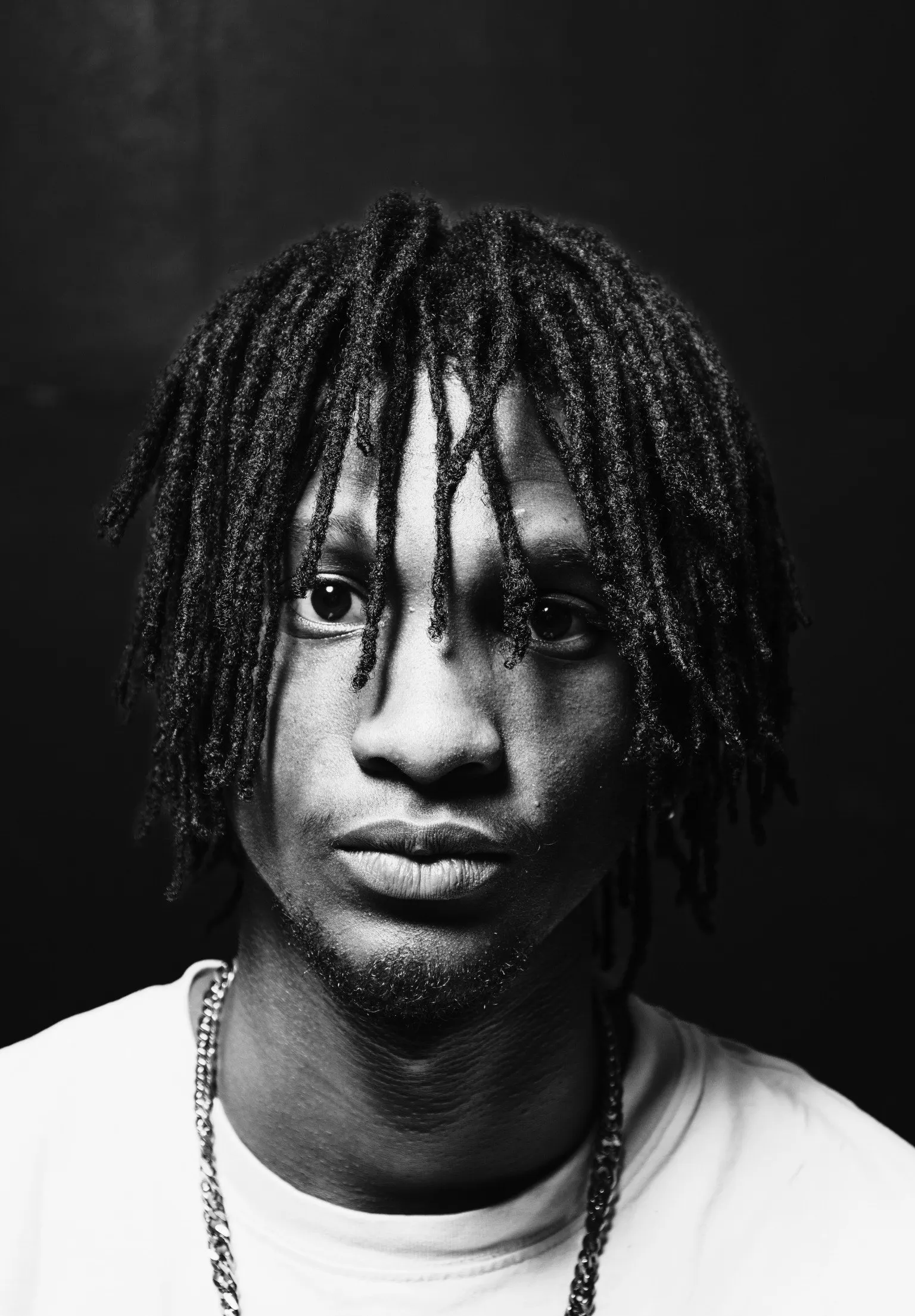 Black and white portrait of a young man with dreadlocks and a white shirt looking straight into the camera