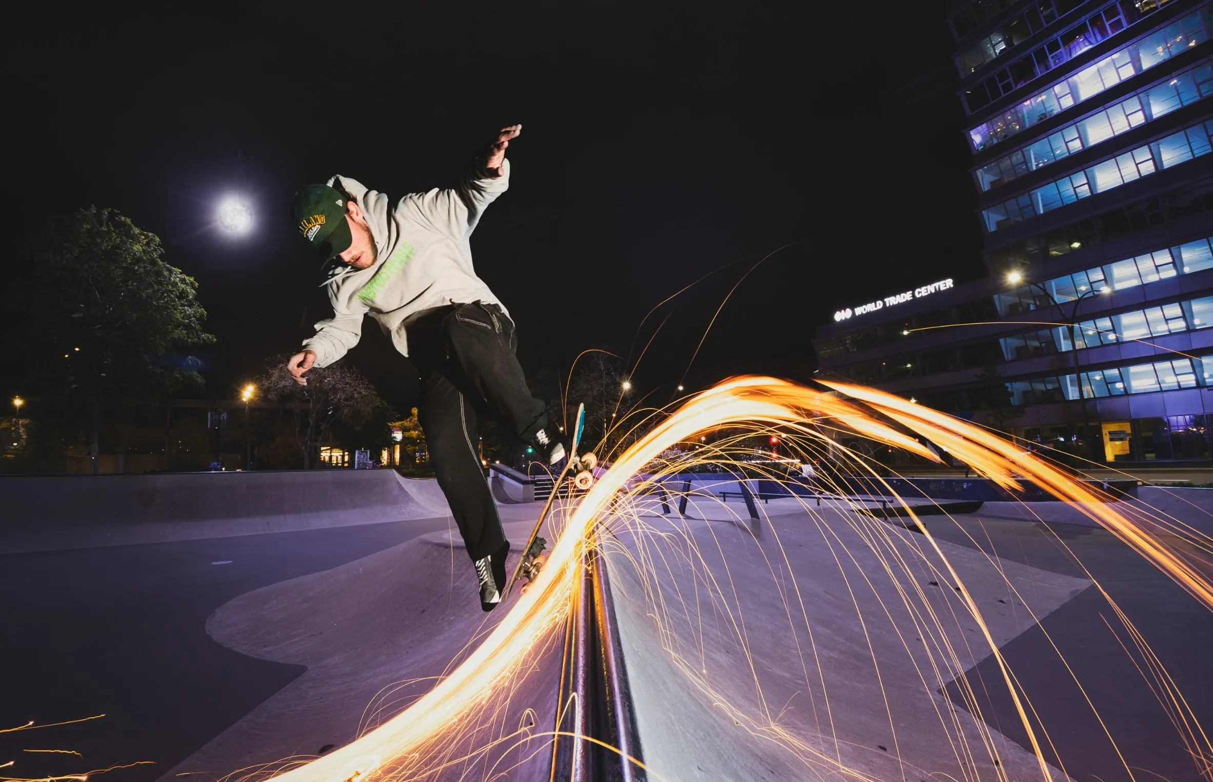 Skater jumping off a ledge at night as a trail of sparks lights up behind him, office buildings in the background