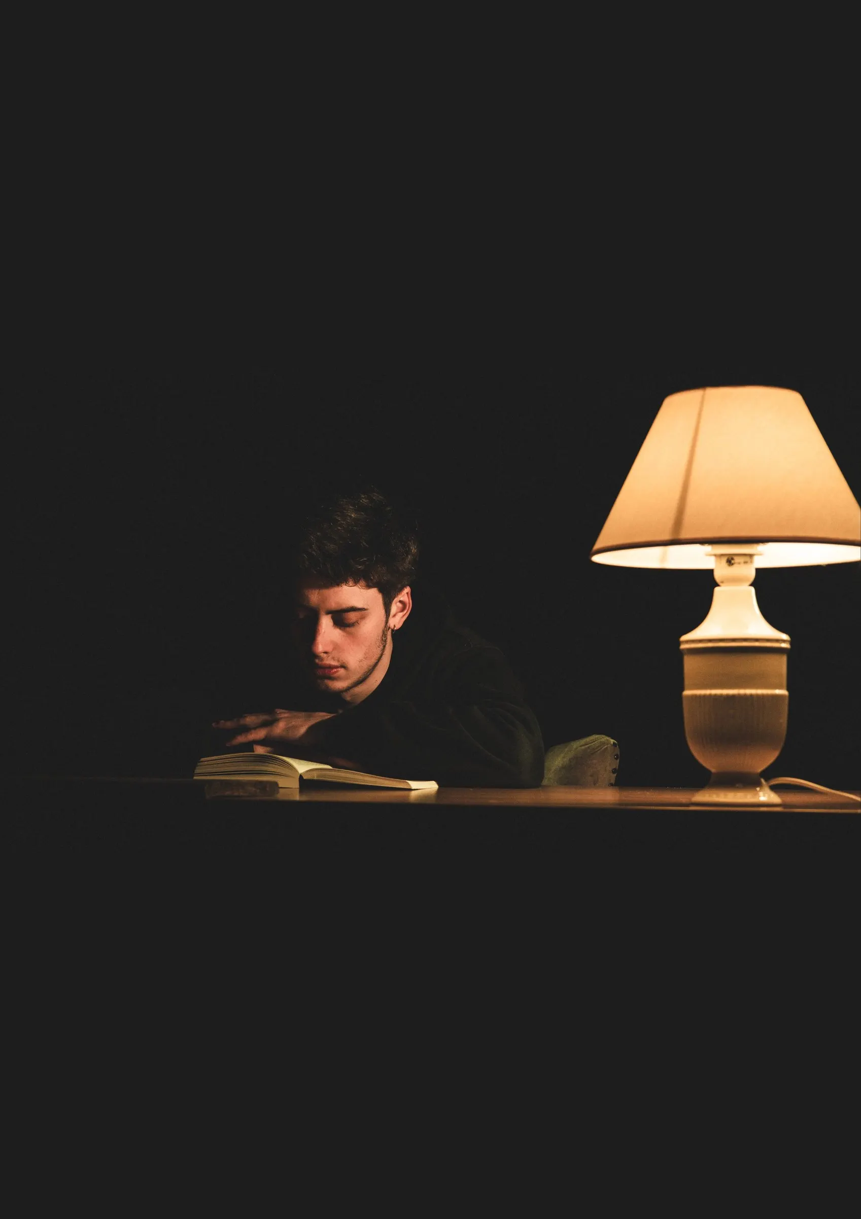 Young man reading at a table in the evening, lit only by a table lamp