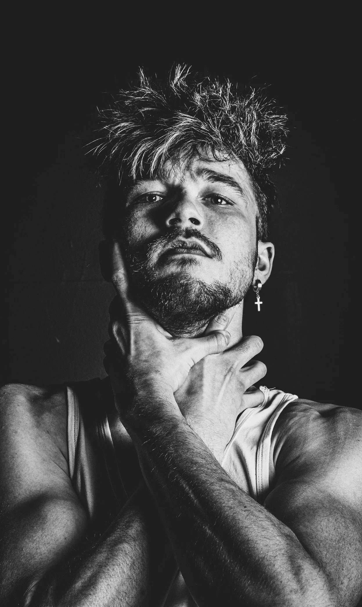Black and white portrait of a man with tousled hair and a beard, eyes half closed, his hand at his throat, against a dark background